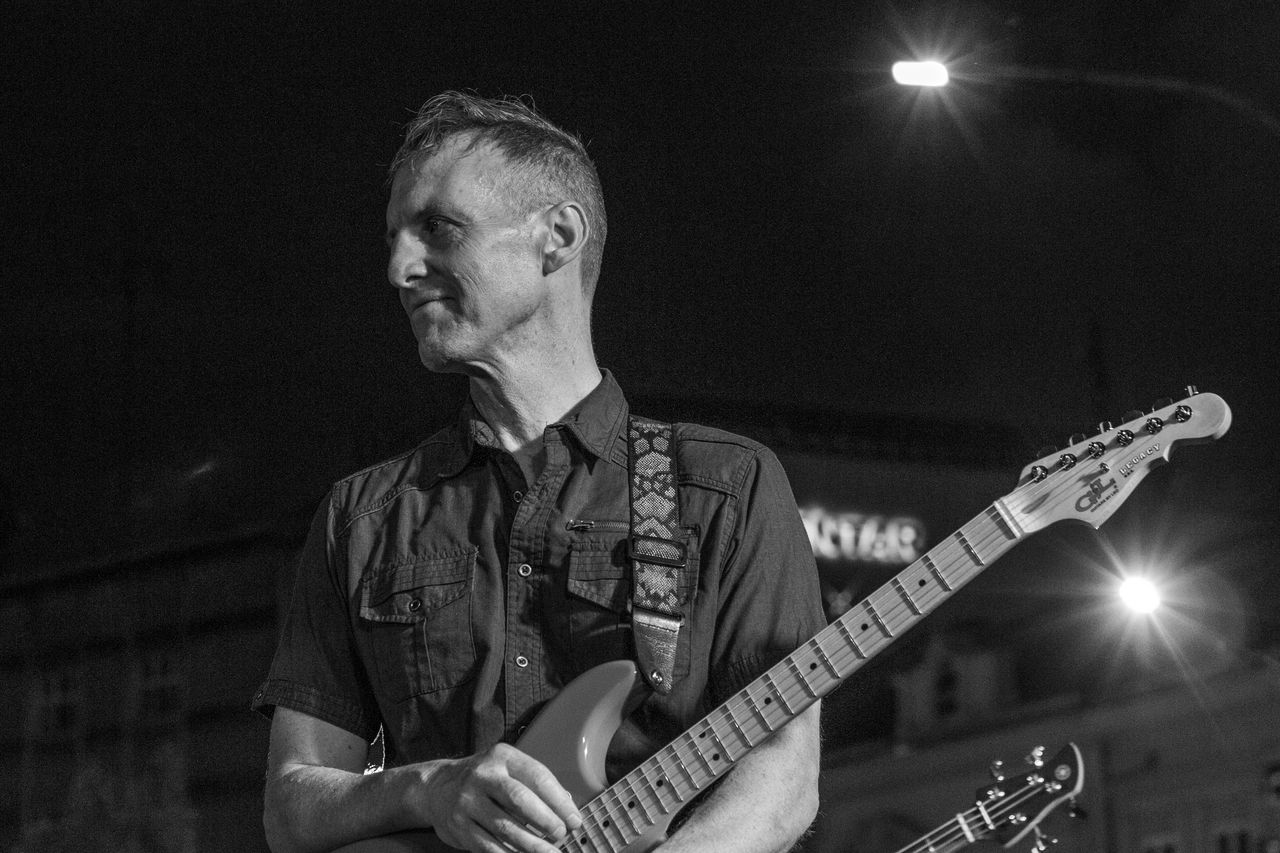Crno-bijeli portret gitarista i pjevača ADONAI-ja za mikrofonom.